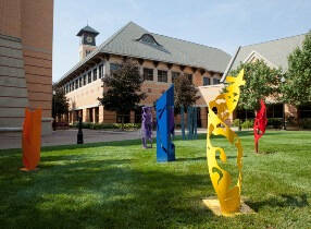 Colorful sculptures in a grassy area with brick buildng in the background.